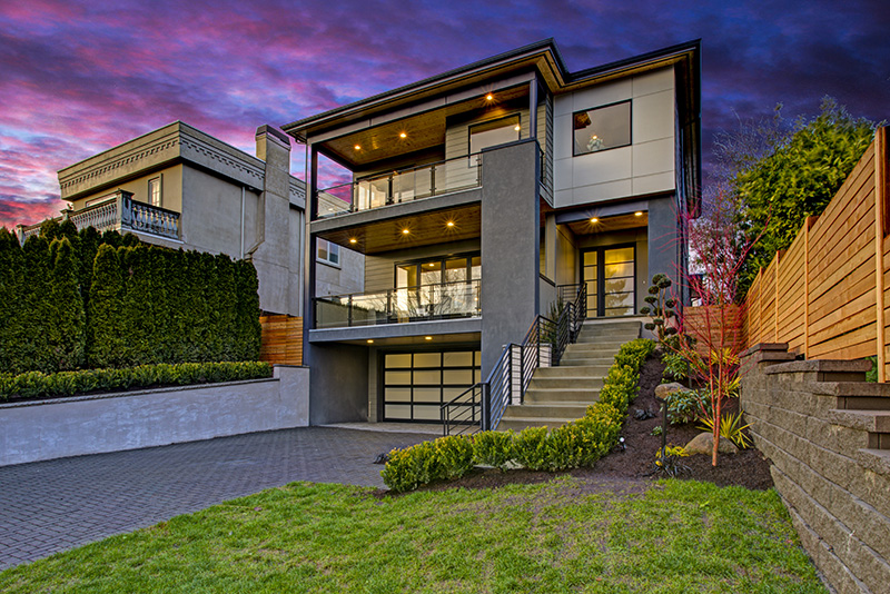 Luxury modern home exterior at sunset boasts four car garage with wide driveway.